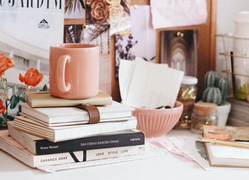 Books piled up on a table. A mug kept above them.